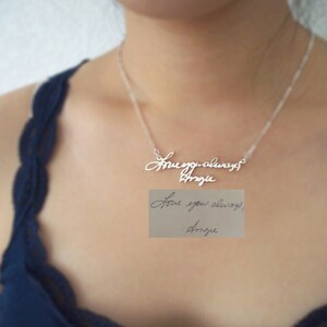 May include: A silver necklace with a handwritten inscription that reads "Love you always Angie". The inscription is on a silver chain and is worn by a person with a blue top.