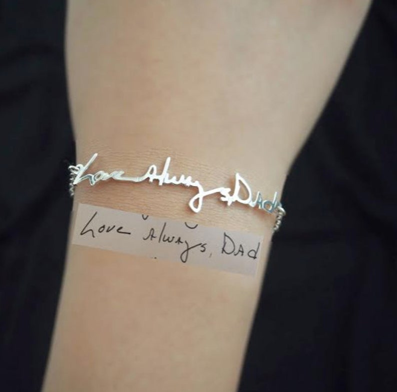 May include: A silver bracelet with a handwritten inscription that reads "Love Always Dad". The inscription is on a piece of paper with the same handwriting.