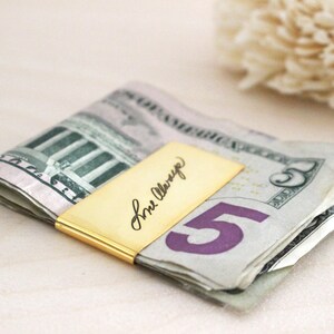 May include: A gold money clip with the inscription "For Always" on a stack of US dollar bills.