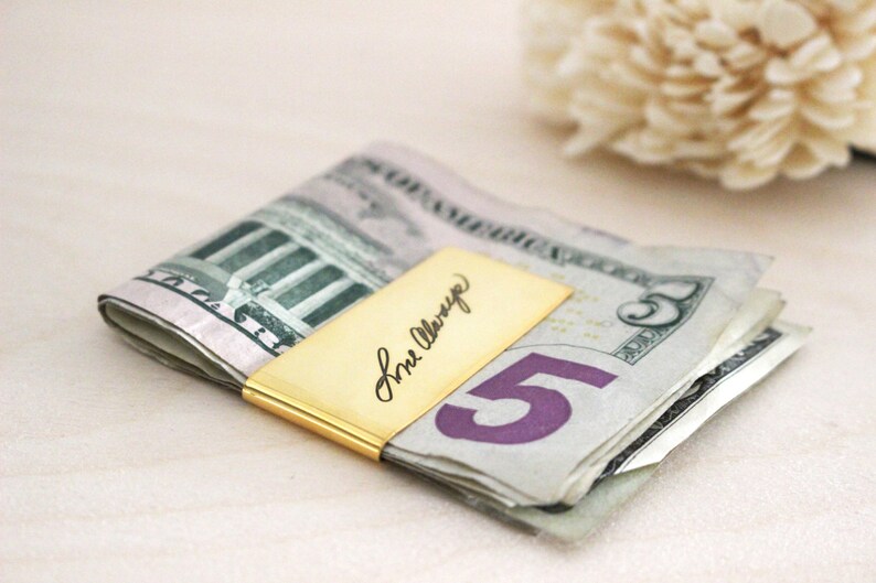 May include: A gold money clip with the inscription "For Always" on a stack of US dollar bills.
