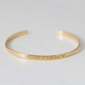 May include: Gold bangle bracelet with the coordinates "36.776° N 119.42° W" engraved on the front.