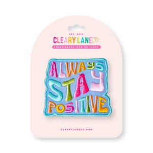 May include: A blue iron-on patch with the text "Always Stay Positive" in colorful, stylized lettering. The patch is packaged on a white card with the company name "Cleary Lane Co." and the text "Embroidered Iron On Patch".