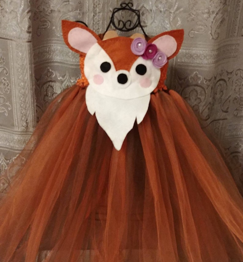 An orange and brown tulle tutu dress with a deer applique. The deer has white fur, pink ears, pink cheeks and a black nose. The deer applique is decorated with purple flowers.