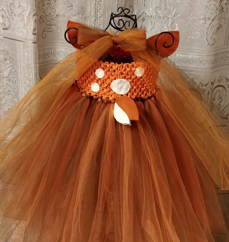 A brown tulle tutu dress with a white deer spots on the back of the bodice and a brown felt deer tail. The dress has brown tulle straps that can tie at the neck or back of the dress.