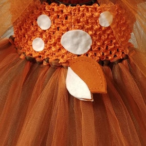 Back side view of the dress.  Orange and brown tulle tutu with a crocheted bodice and white felt polka dots. The bodice has a brown felt bow with a brown and white deer tail accent.