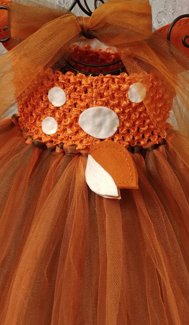 Back side view of the dress.  Orange and brown tulle tutu with a crocheted bodice and white felt polka dots. The bodice has a brown felt bow with a brown and white deer tail accent.