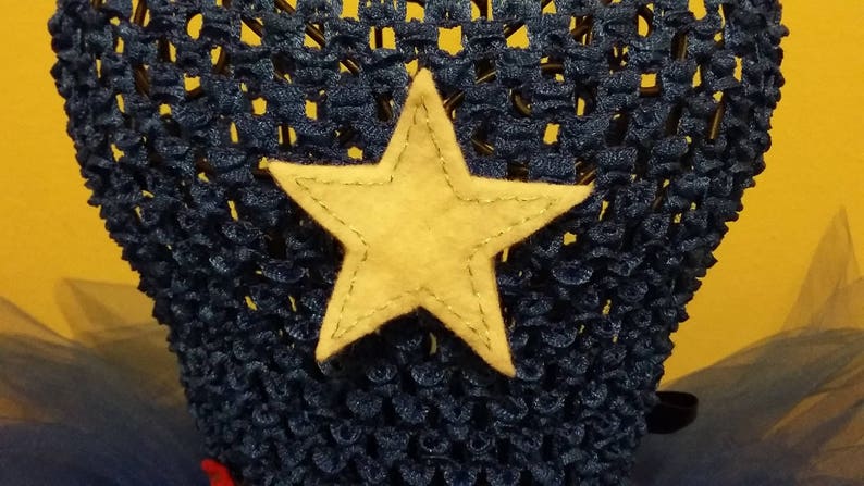 Op de afbeelding: Een donkerblauwe gehaakte hoofdband met een grote, lichtgele sterapplicatie. De ster is op de hoofdband genaaid. De hoofdband is waarschijnlijk voor een kind en staat tegen een gele achtergrond.