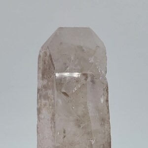 May include: A clear quartz crystal with a double termination and a natural, rough exterior. The crystal is approximately 5 inches tall and has a slightly reddish hue at the base.