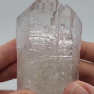 May include: A clear quartz crystal with a double termination and iridescent rainbow inclusions. The crystal is approximately 2 inches tall and has a natural, rough texture.