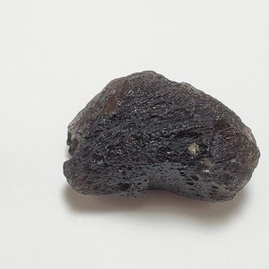 Peut inclure: Une roche de couleur gris foncé, de forme irrégulière, avec une surface rugueuse et texturée. La roche mesure environ 1 cm.