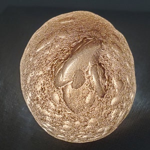 May include: A gold-coloured, round, textured ornament with a raised, textured design on the top.