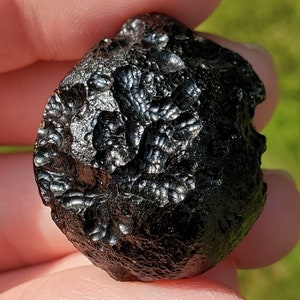 May include: A black, round, textured rock with a unique, intricate pattern. The rock has a smooth, polished surface and appears to be a meteorite.