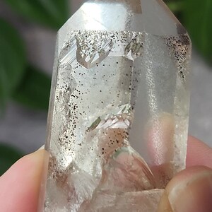 May include: A clear quartz crystal with a double termination and inclusions of black tourmaline. The crystal is approximately 2 inches tall and has a natural, rough texture.