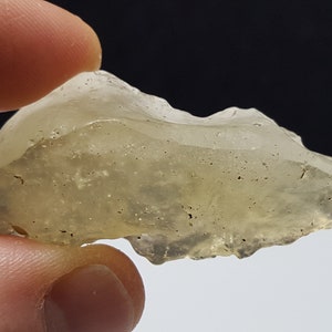 May include: A translucent, light yellow, irregularly shaped piece of glass with dark flecks throughout.