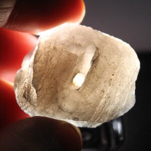 Pode incluir: Um close-up de uma rocha branca opaca de forma irregular com um buraco no centro. A rocha é translúcida e tem uma textura áspera.