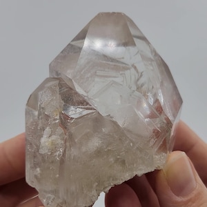 Könnte beinhalten: Ein klarer Quarzkristall-Cluster mit mehreren Spitzen und Facetten. Der Kristall ist durchscheinend und hat einen leichten Schimmer.