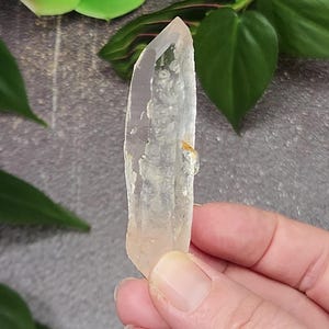 Op de afbeelding: Een heldere kwartskristalpunt met een lichtroze tint en insluitsels. De kristal is ongeveer 5 cm lang en heeft een puntige punt.