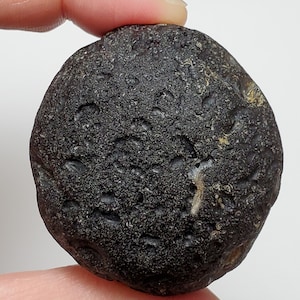 Könnte beinhalten: Ein runder, glatter Stein in Dunkelgrau mit einer strukturierten Oberfläche. Der Stein hat einen hellgrauen Streifen, der durch ihn verläuft.