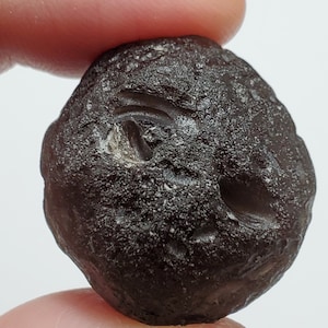 May include: A dark brown, smooth, round stone with a white, circular pattern on the surface.