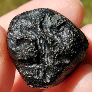 May include: A black, irregularly shaped meteorite with a rough, textured surface. The meteorite has a metallic sheen and appears to be made of iron.