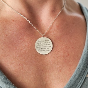 Model in teal and white striped shirt is wearing large round silver necklace with large round pendant, engraved on front with Scripture verse in 6 lines of text.