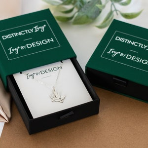 DistinctlyIvy IvyByDesign green drawer gift box - two boxes laying on brown paper and satin fabric with green leaves in the background.  One box is open showing a white IvyByDesign necklace card with a silver bearded dragon necklace on top