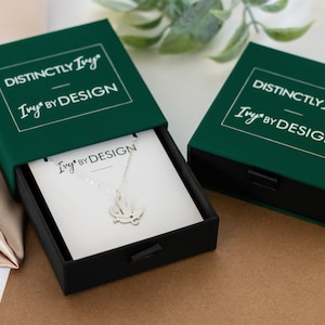 DistinctlyIvy IvyByDesign green drawer gift box - two boxes laying on brown paper and satin fabric with green leaves in the background.  One box is open showing a white IvyByDesign necklace card with a silver bearded dragon necklace on top