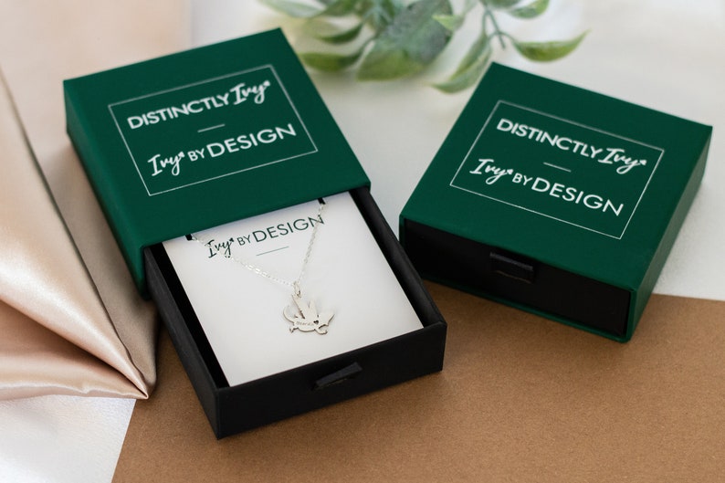 DistinctlyIvy IvyByDesign green drawer gift box - two boxes laying on brown paper and satin fabric with green leaves in the background.  One box is open showing a white IvyByDesign necklace card with a silver bearded dragon necklace on top