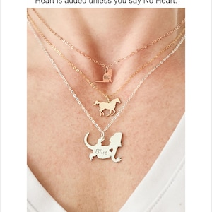 Model is shown with white shirt wearing a rose gold cat necklace, gold running horse necklace, and silver bearded dragon necklace, engraved with the name Blue.  All pendants are different sizes. All chains are different lengths for a layered look.