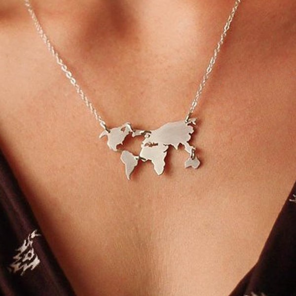 May include: A silver necklace with a world map pendant. The pendant is a detailed outline of the continents. The necklace is worn against a dark brown top with a white patterned design.