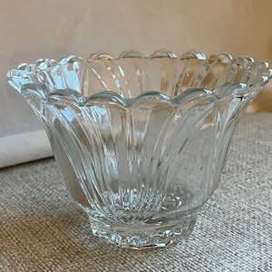 May include: A clear glass bowl with a scalloped rim and a fluted design. The bowl is empty and has a shiny finish.