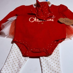 May include: A red baby bodysuit with the word "Christmas" in white script, paired with a matching red bonnet and white leggings with gold polka dots. The bodysuit has a tulle skirt. The set is displayed on a hanger.