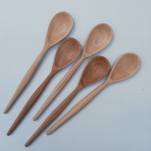 May include: Five wooden spoons of varying lengths and shades of brown, arranged in a fan shape on a white background.