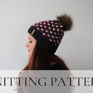 May include: A knitting pattern for a burgundy and grey beanie with a white heart pattern and a brown faux fur pom pom.