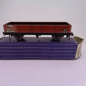 May include: A red toy train wagon with the words "TUBE 20T W73349 XP 8-0-0" printed on the side. The wagon is sitting on a blue box with the words "TUBE WAGON" printed on the side.