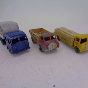 May include: Three vintage toy trucks, a blue garbage truck, a red and yellow dump truck, and a yellow truck with a load of "Portland Cement" boxes.