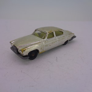 May include: A silver toy car model of a Jaguar sedan. The car has a yellowed interior and black wheels.