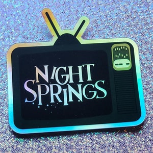 May include: A holographic sticker depicting a vintage television set. The screen shows the words "NIGHT SPRINGS" in a decorative font. The sticker has a black outline and aerials, with a shimmering, iridescent finish.