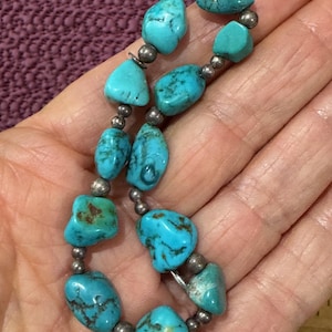 May include: A turquoise stone bracelet with silver-colored beads. The bracelet features irregularly shaped, vibrant blue-green turquoise stones. The stones are strung together with small, round silver-colored beads, creating a unique and eye-catching accessory.