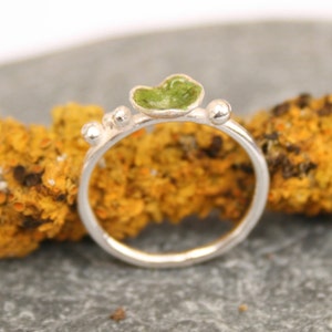 May include: A silver ring with a green stone set in the centre. The ring is decorated with small silver beads.