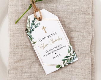May include: A white rectangular favor tag with a gold geometric border, green watercolor eucalyptus leaves, and a gold cross. The text reads: GOD BLESS, Tyler Charles, THANK YOU FOR CELEBRATING WITH US!, and 06.12.21. A brown twine loop is attached.