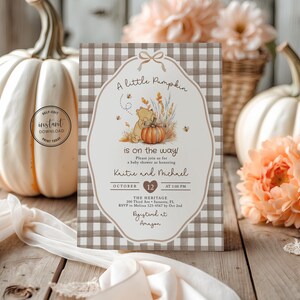 May include: A rectangular baby shower invitation card featuring a brown and white gingham border and a central illustration of a bear with a pumpkin. The text reads A little Pumpkin is on the way, honouring Kaitie and Michael on October 12.