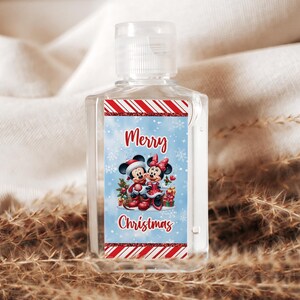 May include: A clear, rectangular hand sanitizer bottle with a white cap. The label features Mickey and Minnie Mouse in Christmas attire, with the words "Merry Christmas" in red script. Red and white striped borders frame the label.