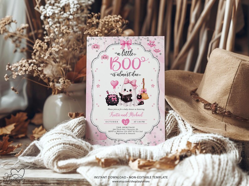 May include: A rectangular baby shower invitation card featuring a pink and white theme with a ghost illustration, a black cauldron, a broom, and a heart-shaped balloon. The text reads a little BOO is almost due, honoring Kaitie and Michael.