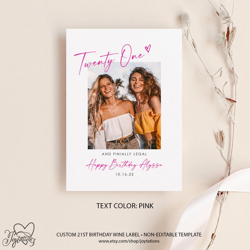 May include: A pink and white printable 21st birthday wine label template with a photo of two women smiling. The text reads "Twenty One" with a pink heart, "And Finally Legal", "Happy Birthday Alyssa", and "10.16.22". The text color is pink.