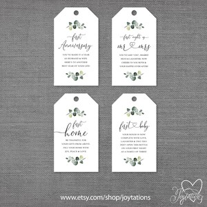 May include: Four white gift tags with green eucalyptus leaves and black calligraphy. The tags read "first anniversary", "first night as mr & mrs", "first home", and "first baby".