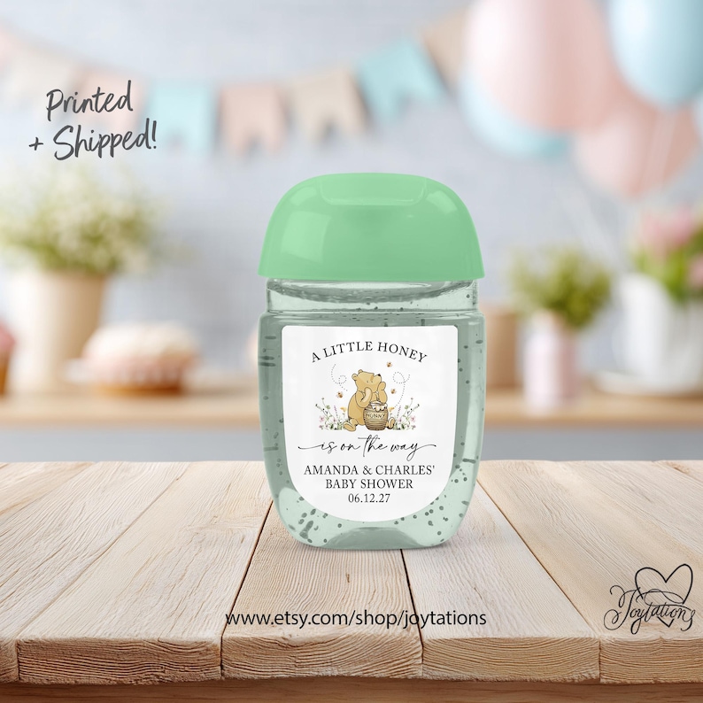 May include: A clear plastic hand sanitizer bottle with a light green flip-top cap. The label features a Winnie the Pooh illustration, the text A LITTLE HONEY is on the way, AMANDA & CHARLES' BABY SHOWER, and the date 06.12.27.