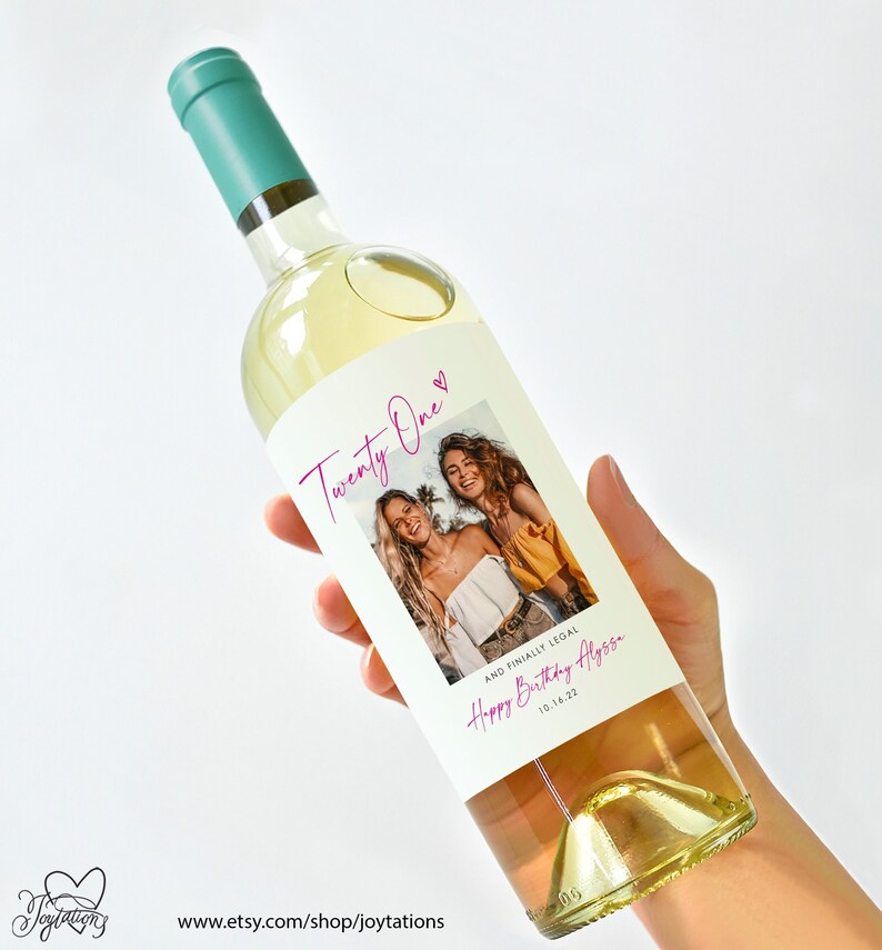May include: White wine bottle with a custom label. The label features a photo of two women, the text "Twenty One" with a pink heart, and the text "And finally legal. Happy Birthday Alyssa 10.14.22".