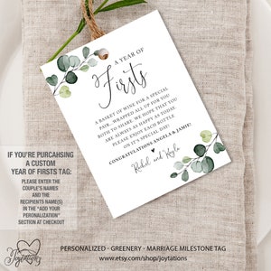 May include: A white tag with green eucalyptus leaves and the text "A Year of Firsts" with a basket of wine for a special pair. The text also includes "Congratulations Angela & Jamie!" and "Rachel and Kayla".