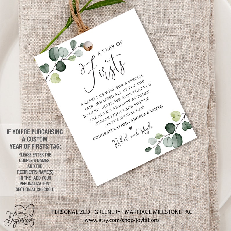 May include: A white tag with green eucalyptus leaves and the text "A Year of Firsts" with a basket of wine for a special pair. The text also includes "Congratulations Angela & Jamie!" and "Rachel and Kayla".